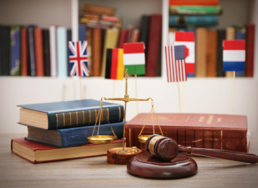 Imagem colorida de escritório de advogacia em Direito Internacional, com livros  e balança jurídica sobre uma mesa e ao fundo bandeiras de diferentes países.
